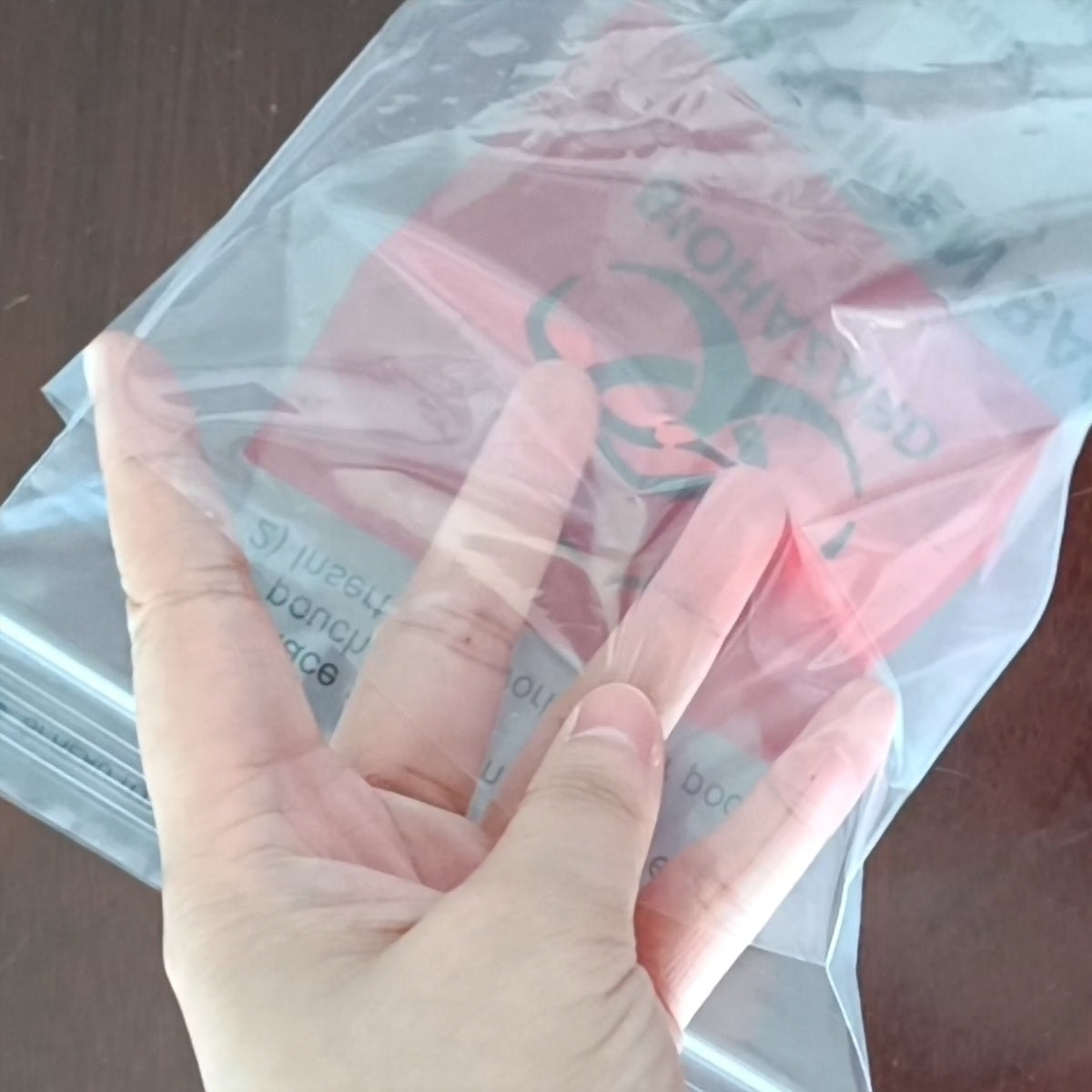 CliniEco Medical 6 x 9 in 95 kPa specimen transport bag held in hand — clear outer pouch with red biohazard inner bag